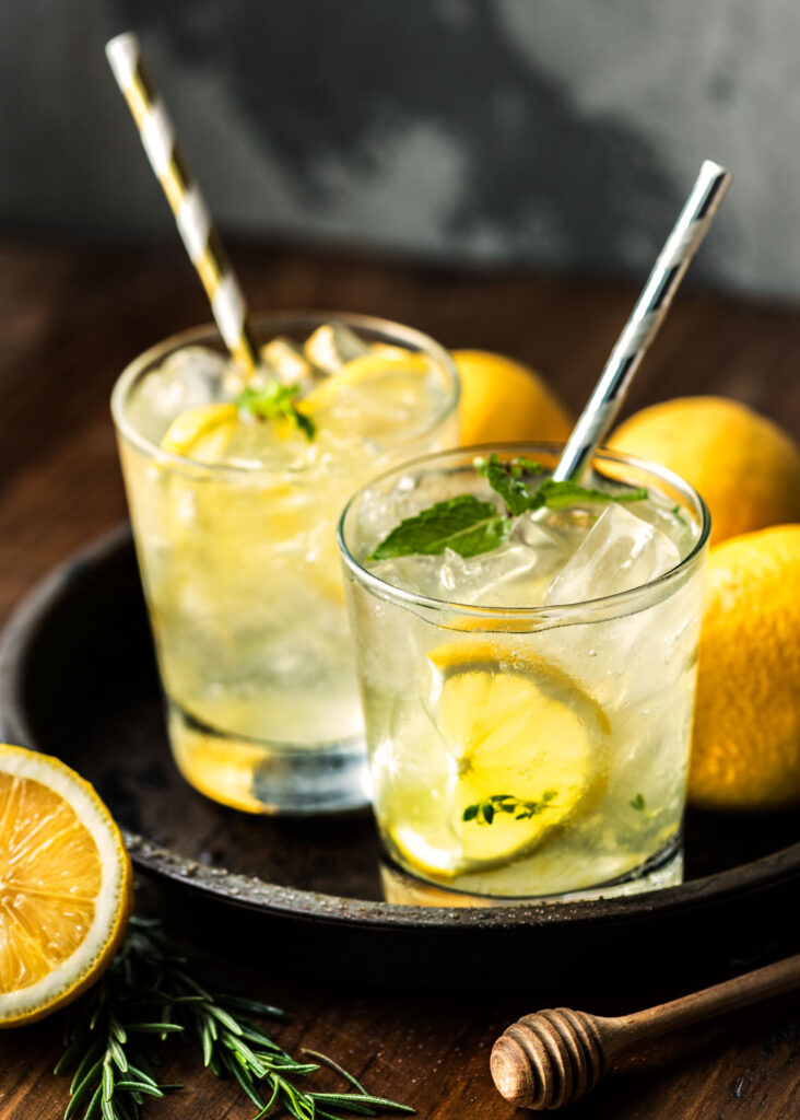 Zwei Gläser Limoncello Spritz mit Eiswürfeln, Zitronenscheiben und Minze auf einem Tablett – erfrischender Sommerdrink mit italienischer Zitrone.