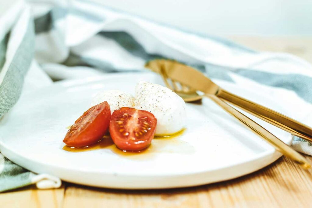 Frischer Mozzarella di Bufala mit Tomaten und Olivenöl auf einem weißen Teller – klassisches italienisches Antipasto mit Mozzarella.