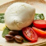 Große Mozzarella di Bufala auf Babyspinat mit Tomaten und Oliven – Mozzarella-Delikatesse aus Kampanien.