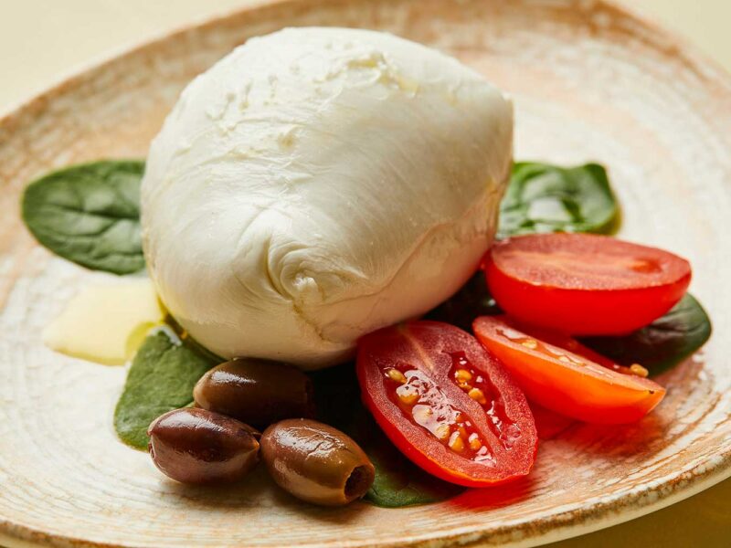 Große Mozzarella di Bufala auf Babyspinat mit Tomaten und Oliven – Mozzarella-Delikatesse aus Kampanien.