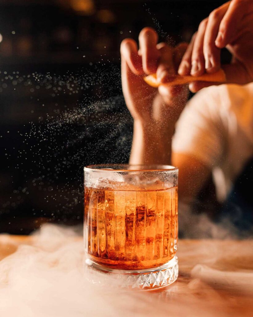 Negroni-Cocktail mit Eis im klassischen Glas, während eine Orangenzeste frisch über dem Drink gespritzt wird, um die Aromen zu intensivieren.