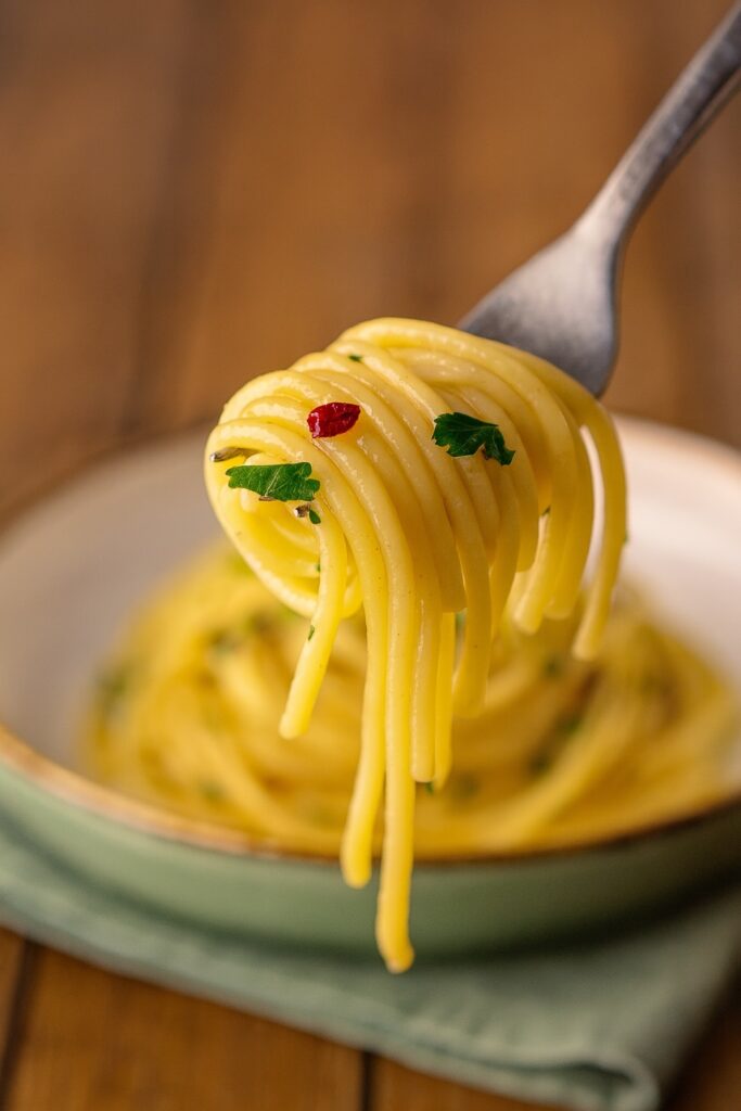 Nahaufnahme einer Gabel mit aufgerollten Spaghetti Aglio, Olio e Peperoncino, garniert mit Petersilie und Chilistückchen.