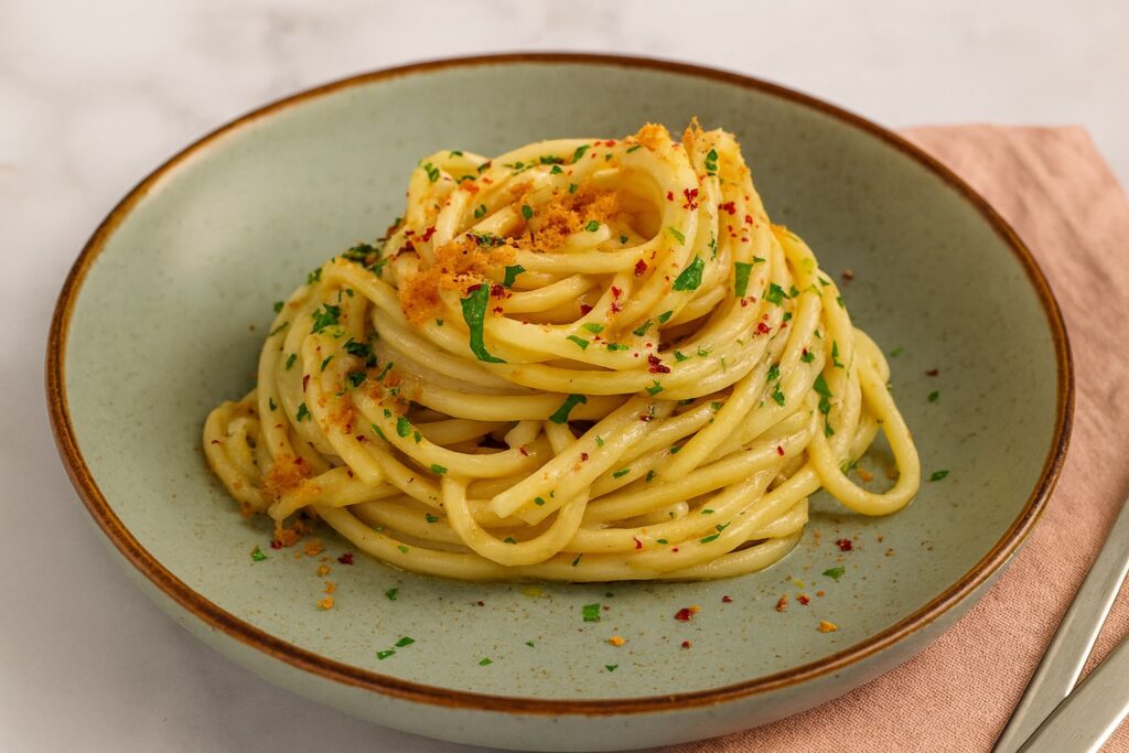 Moderne Interpretation von Spaghetti Aglio, Olio e Peperoncino mit knusprigen Bröseln und fein gehacktem Peperoncino auf grünem Keramikteller.