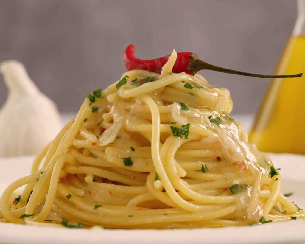 Nahaufnahme eines Tellers mit Spaghetti Aglio, Olio e Peperoncino, garniert mit frischer Petersilie und einer ganzen Chilischote.