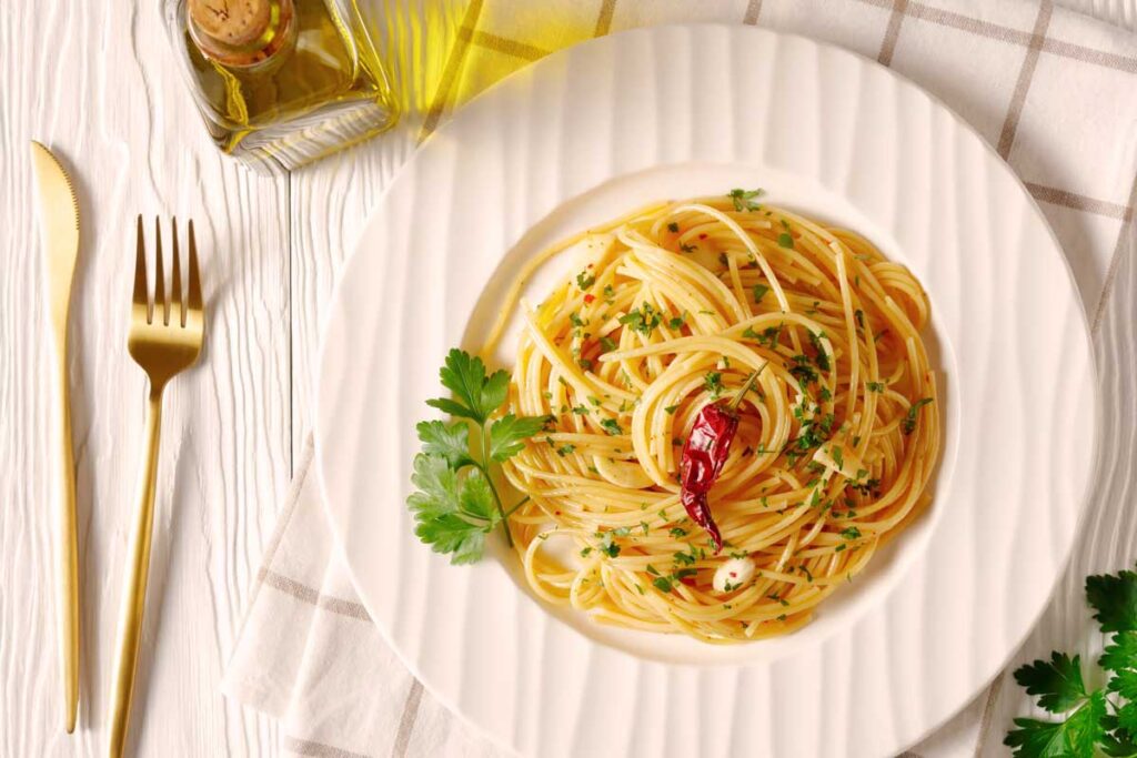 Ansicht von oben auf perfekt angerichtete Spaghetti Aglio, Olio e Peperoncino mit Petersilie und Chilischote auf weißem Teller.
