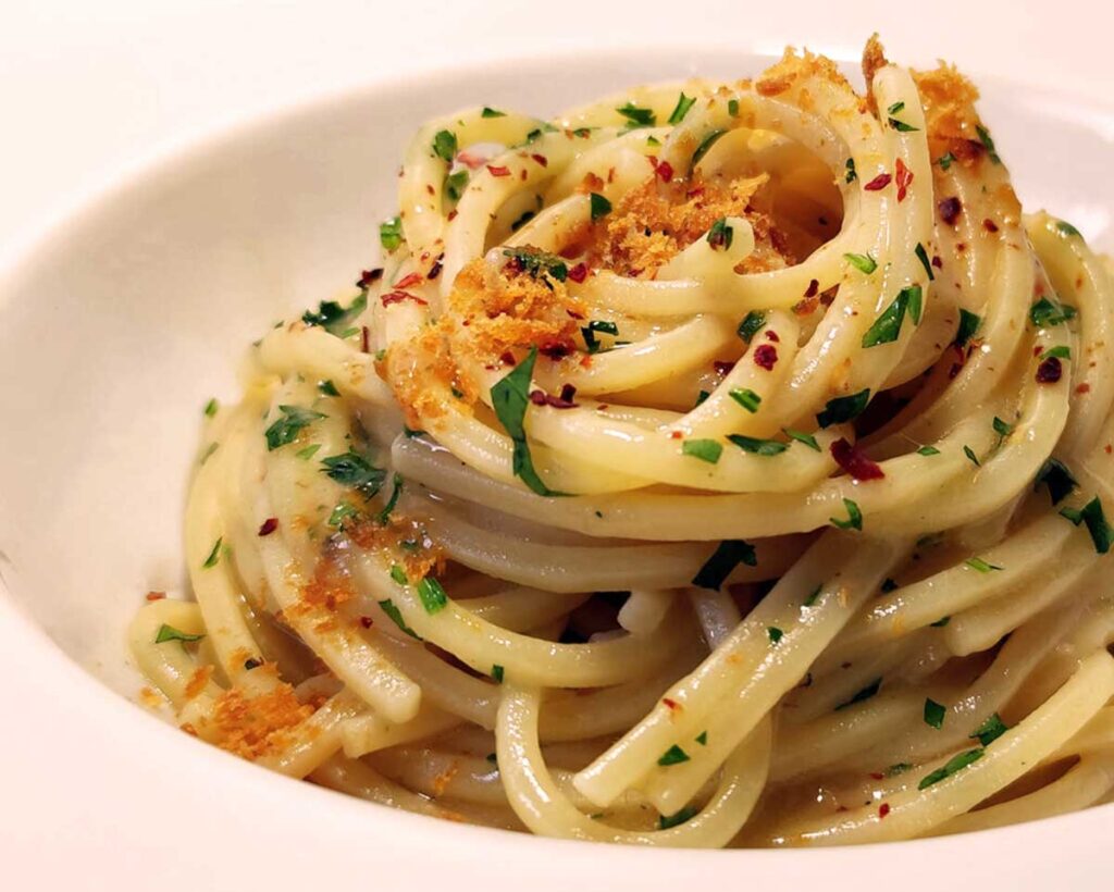 Cremige Spaghetti Aglio, Olio e Peperoncino mit knusprigen Bottarga und frischen Kräutern in einer weißen Schale serviert.