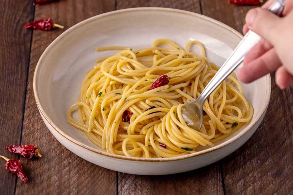 Spaghetti Aglio, Olio e Peperoncino in rustikaler Keramikschale, bereit zum Genießen mit Gabel und getrockneten Chilischoten im Hintergrund.