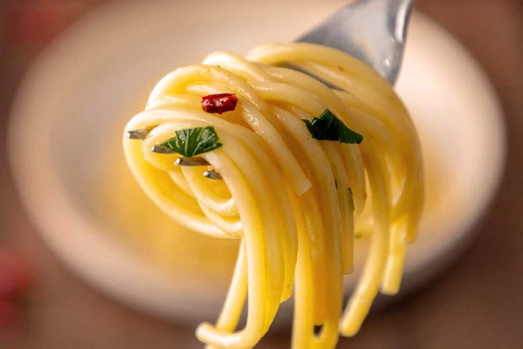 Detailaufnahme von Spaghetti Aglio, Olio e Peperoncino auf einer Gabel, mit Petersilie und Chili für intensives Aroma.