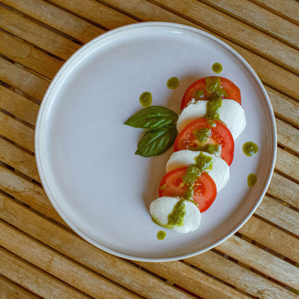 Minimalistisch angerichteter Caprese-Salat mit Tomaten, Mozzarella und Basilikum-Pesto auf einem weißen Teller auf Holzuntergrund.