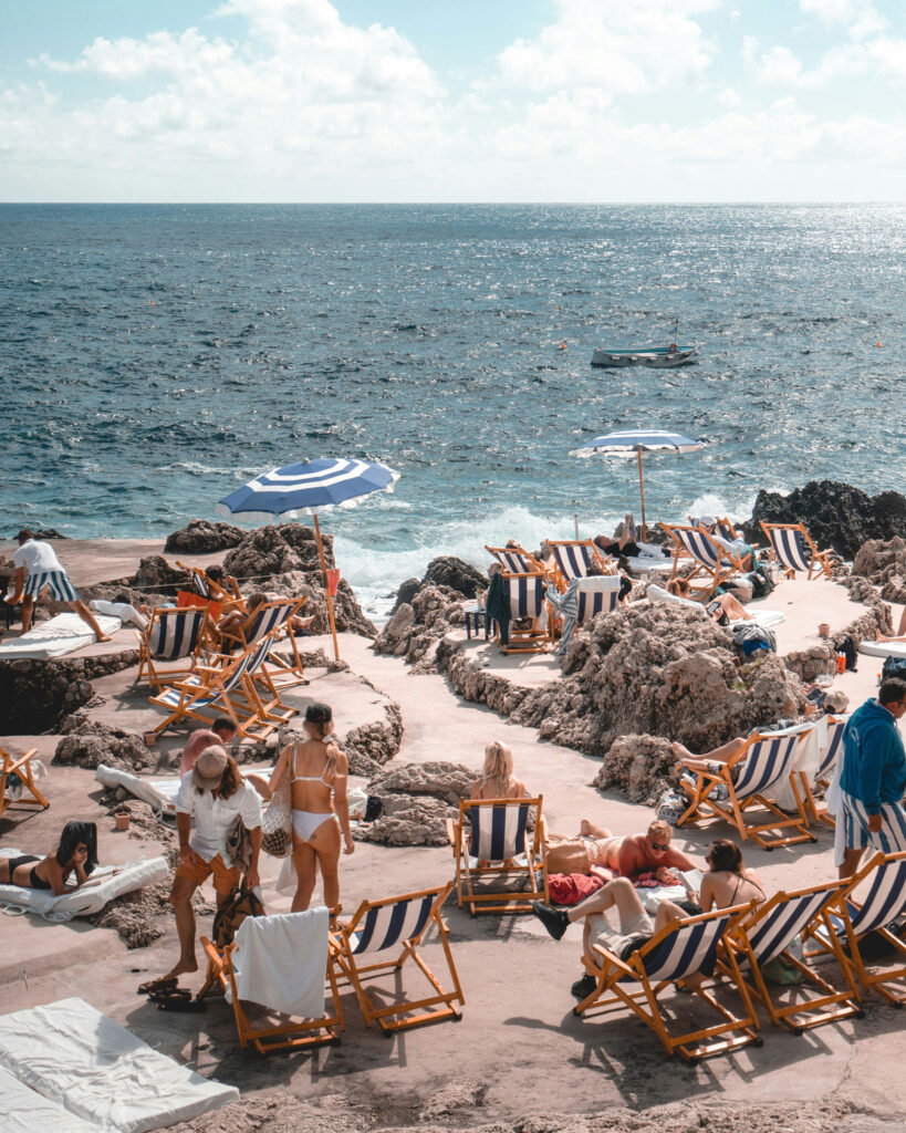 Strandatmosphäre auf Capri mit Sonnenliegen und Sonnenschirmen direkt am Felsenmeer – das perfekte Sommerfeeling zum Caprese-Salat.