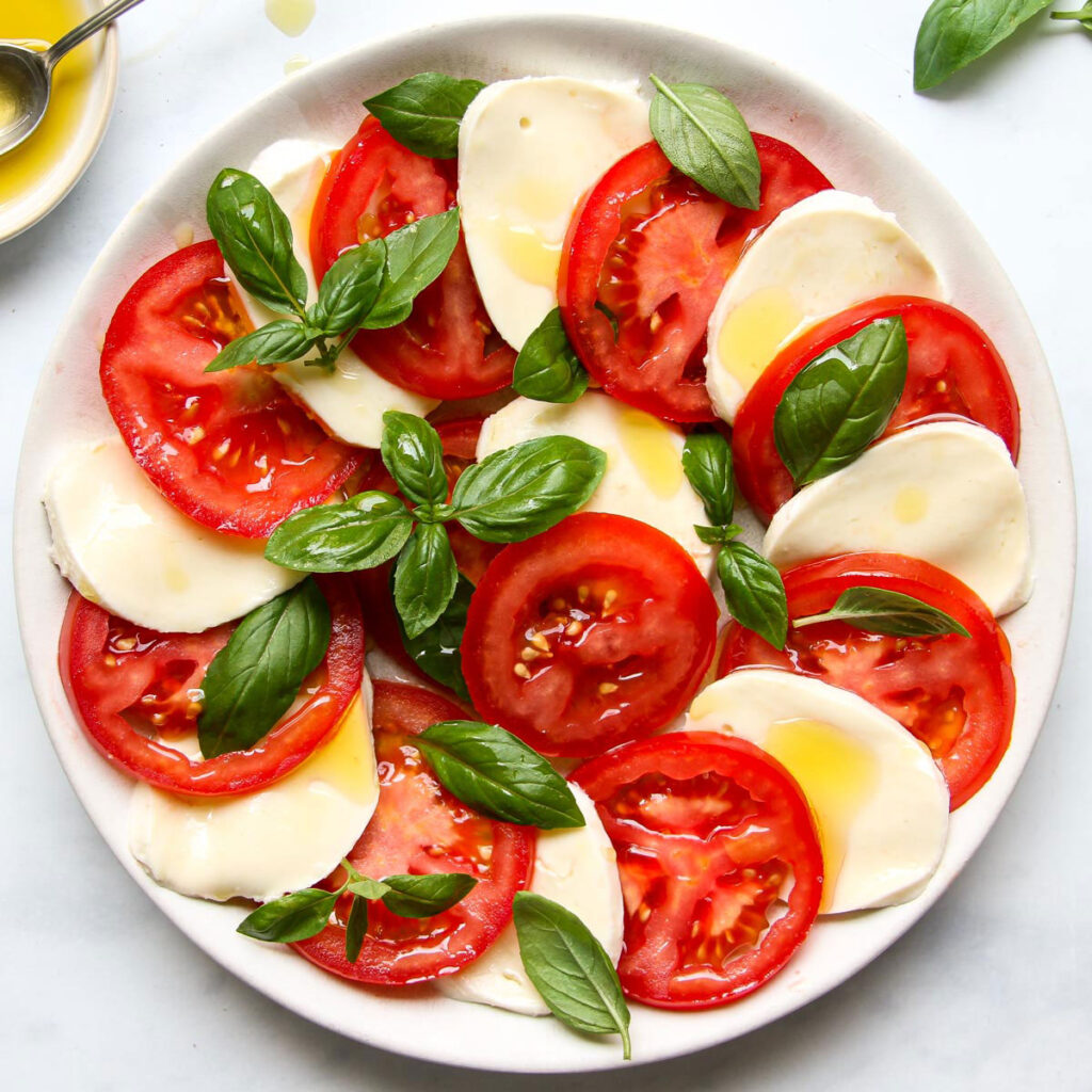 Klassischer Caprese-Salat mit gleichmäßig geschnittenen Tomaten und Mozzarella, garniert mit frischem Basilikum und Olivenöl.