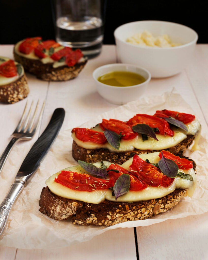 Getoastetes Brot mit geschmolzenem Mozzarella, Ofentomaten und violettem Basilikum – Caprese als Bruschetta-Variation.