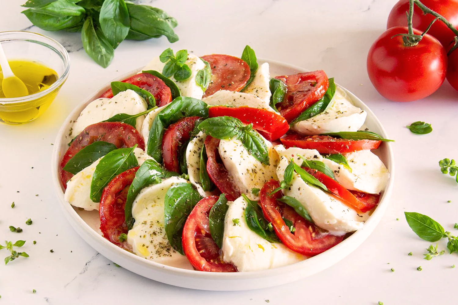 Modern angerichteter Caprese-Salat mit Tomaten, Mozzarella, frischem Basilikum und italienischen Kräutern auf weißem Teller.