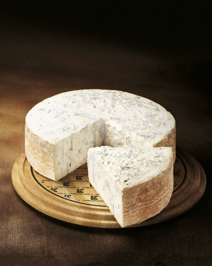 Ein ganzer Laib Gorgonzola DOP mit angeschnittener Spitze auf einem rustikalen Holztablett mit Prägung.