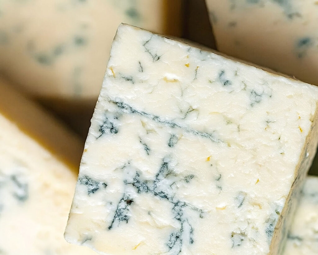 Makroaufnahme eines Gorgonzola-Stücks mit klar sichtbaren blauen Edelschimmelmarmorierungen.