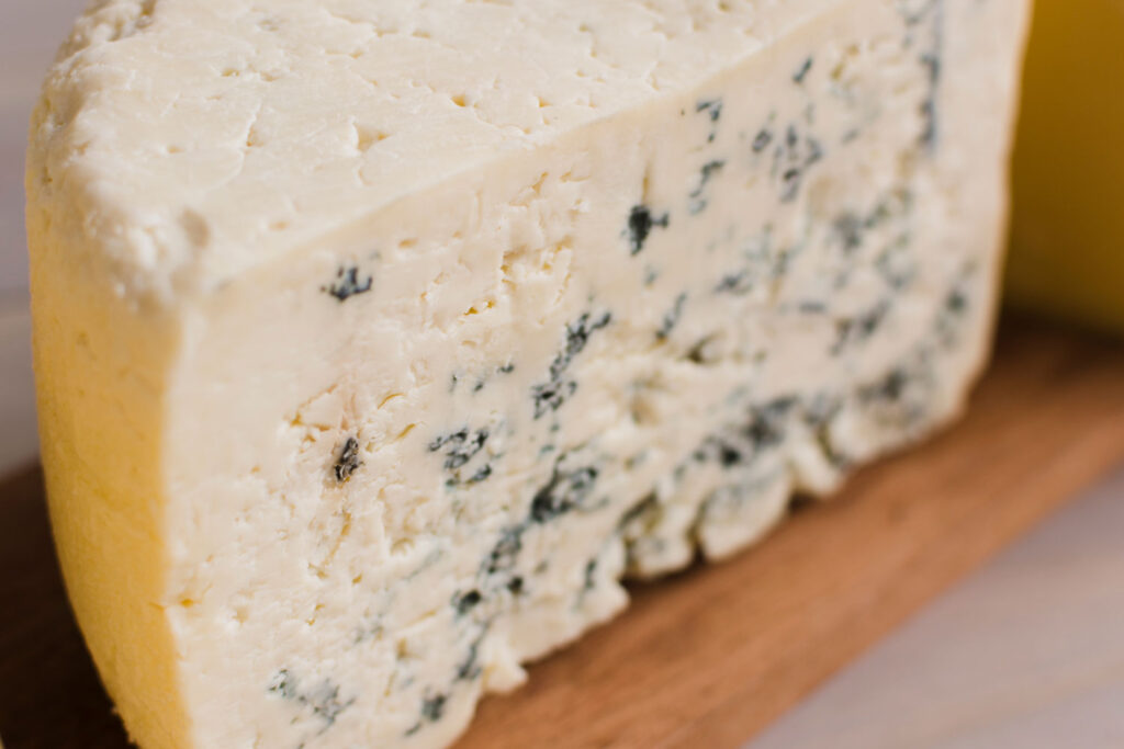 Nahaufnahme eines Gorgonzola-Stücks mit bröckeliger, cremiger Textur und intensiver Blauschimmelmaserung.
