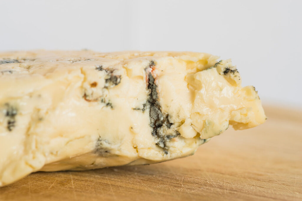 Weicher, cremiger Gorgonzola mit blauen Adern – angeschnitten auf einem Holzbrett vor weißem Hintergrund.