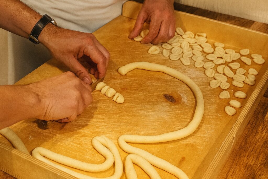 Traditionelle Zubereitung von Orecchiette: Hände formen kleine Teigstücke auf einem Holzbrett.