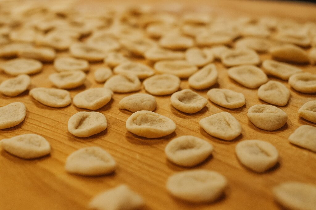 Viele frisch geformte Orecchiette liegen auf einem Holzbrett zum Trocknen ausgebreitet.