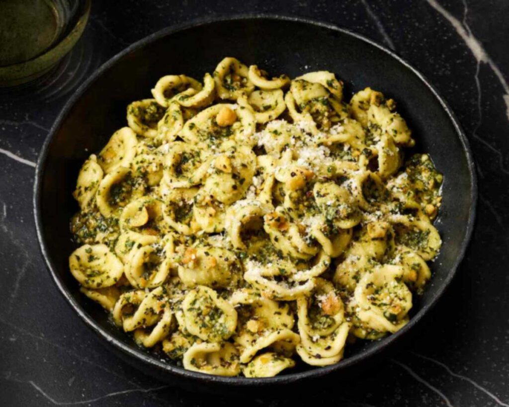 Orecchiette in Pesto alla Genovese mit geriebenem Käse, serviert in einer dunklen Schale auf schwarzem Marmortisch.