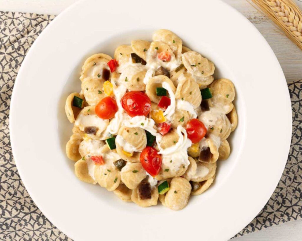 Orecchiette mit bunter Sommergemüse-Mischung und cremiger Sauce, serviert auf einem weißen Teller.