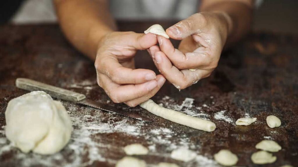 Handwerkliche Herstellung von Orecchiette: Hände formen mit Daumenbewegung kleine Pastaformen aus frischem Teig.