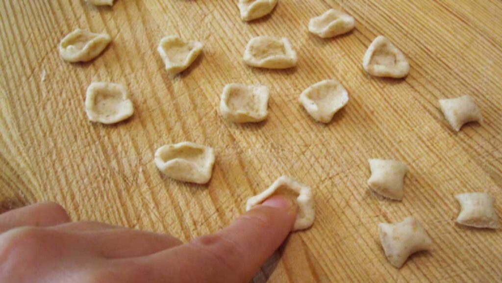 Traditionelle Methode zur Herstellung von Orecchiette: Daumen drückt Teigstückchen zu kleinen Ohrformen.