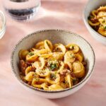 chale mit Orecchiette alla salsiccia – Pasta mit italienischer Wurst, Kräutern und geriebenem Käse auf rosa Untergrund.