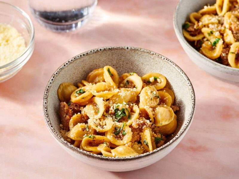 chale mit Orecchiette alla salsiccia – Pasta mit italienischer Wurst, Kräutern und geriebenem Käse auf rosa Untergrund.
