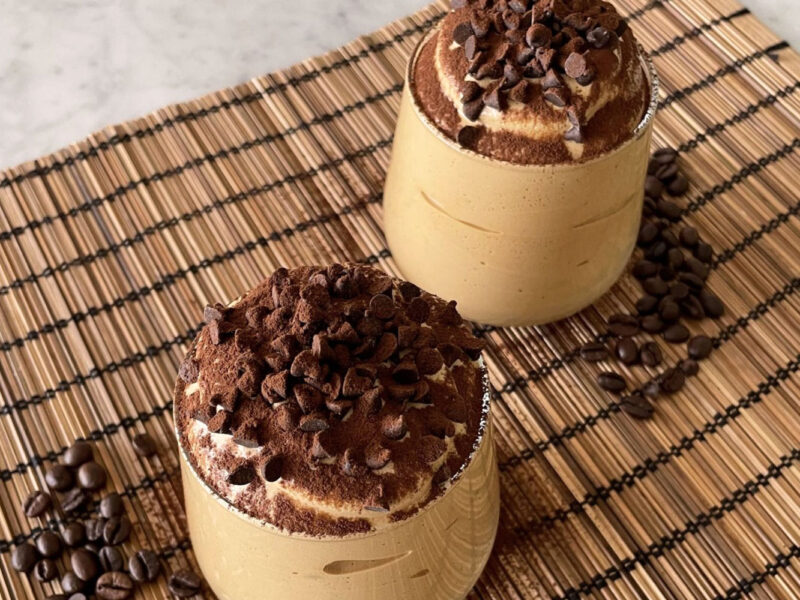 Zwei Gläser Spumone al Caffè mit Sahne, Kakaopulver und Schokosplittern garniert, serviert auf Bambusmatte mit Kaffeebohnen – Dessert mit Wow-Effekt.