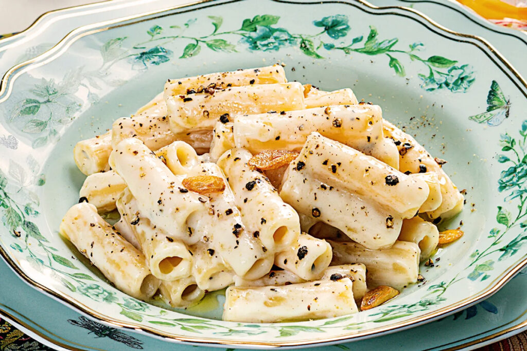 Teller mit Pasta in cremiger Besciamella-Sauce, garniert mit Pfeffer und geröstetem Knoblauch – serviert auf einem dekorativen Porzellanteller
