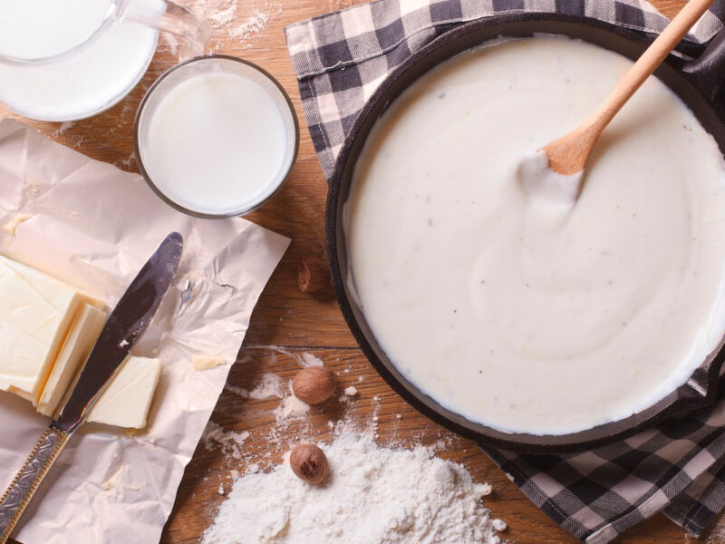 Zubereitung von Besciamella in einer Pfanne, eingerahmt von Butter, Mehl, Milch und Gewürzen – typische Zutaten der italienischen Grundsauce