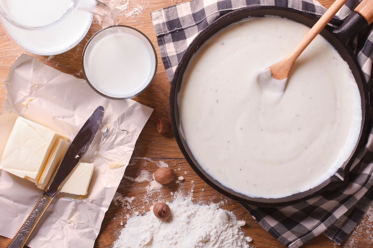 Zubereitung von Besciamella in einer Pfanne, eingerahmt von Butter, Mehl, Milch und Gewürzen – typische Zutaten der italienischen Grundsauce
