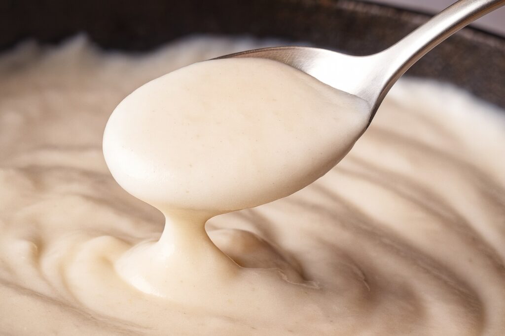 Nahaufnahme eines Löffels mit samtiger Béchamelsauce, perfekt gerührt.