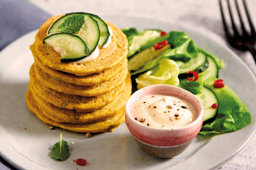 Gestapelte Frittelle di Ceci auf einem Teller mit frischen Gurkenscheiben, Salat und cremigem Dip – ideal als sommerliche Vorspeise oder vegetarischer Snack.