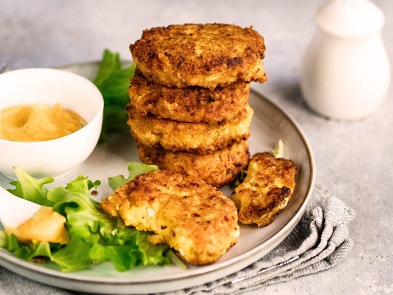 Frittelle di Ceci auf einem hellen Teller kunstvoll gestapelt, begleitet von Senfsauce und frischem Salat – ein Highlight der vegetarischen italienischen Küche.