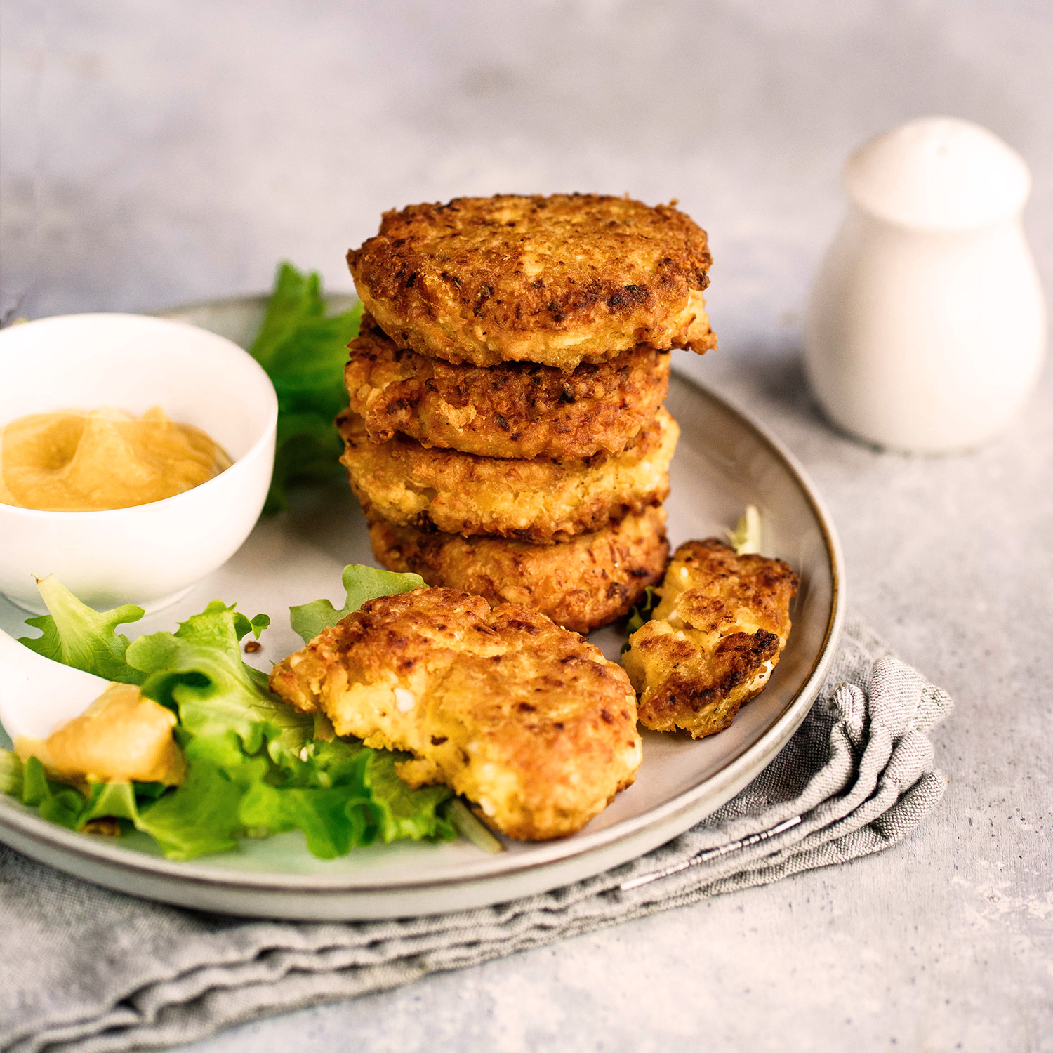 Frittelle di Ceci auf einem hellen Teller kunstvoll gestapelt, begleitet von Senfsauce und frischem Salat – ein Highlight der vegetarischen italienischen Küche.