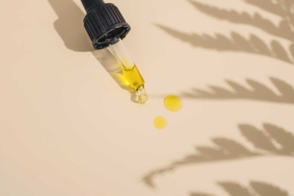 Pipette mit Olivenöl und Tropfen auf hellbeigem Hintergrund mit Blattschatten – hochwertige Kosmetik oder Nahrungsergänzung.