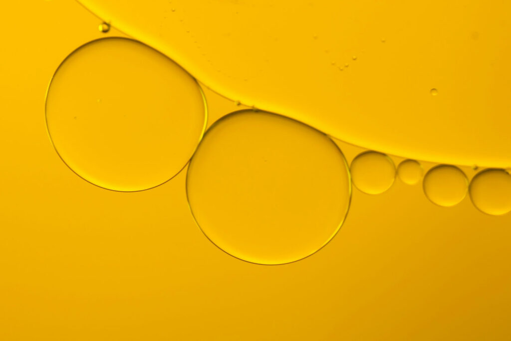 Makroaufnahme von goldgelben Olivenöl-Tropfen auf einer glänzenden Oberfläche – abstrakte Darstellung.
