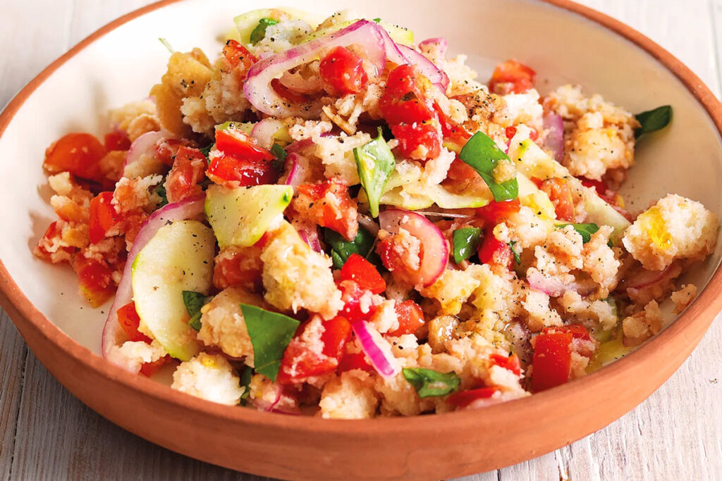 Rustikale toskanische Brotsalat mit Tomaten, roten Zwiebeln, Gurken, Basilikum und Olivenöl in einer Terrakottaschüssel.