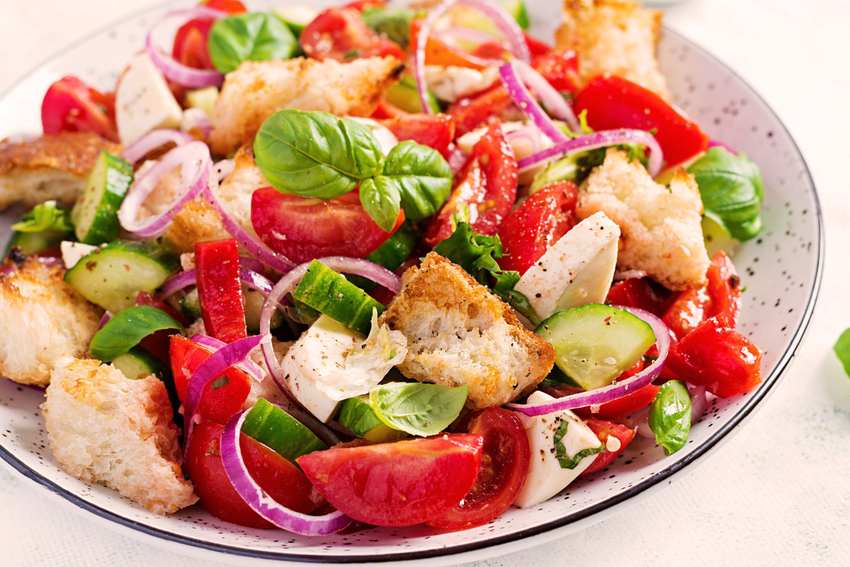 Frische Panzanella mit Tomaten, Gurken, roten Zwiebeln, Mozzarella, Basilikum und knusprigem Brot – serviert auf einem weißen Teller mit schwarzem Rand.