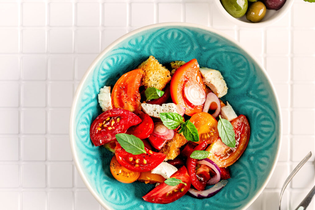 Bunter Panzanella-Salat mit verschiedenen Tomatensorten, Basilikum, Zwiebeln und Brotstücken in türkiser Schale.