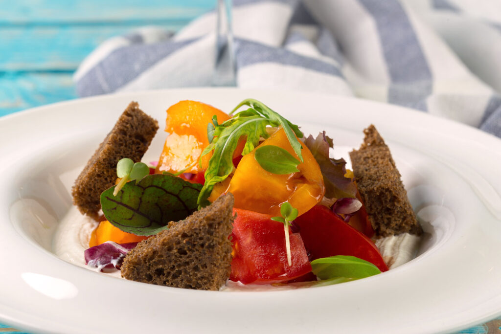 Gourmet-Panzanella mit dunklem Brot, Baby Leaf, gelben Tomaten und Radicchio auf weißem Teller.