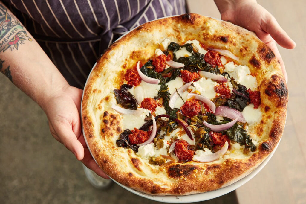 Frisch gebackene Pizza mit Ricotta, Zwiebeln, geschmortem Gemüse und ’Nduja – eine kreative Kombination aus Schärfe und Cremigkeit.