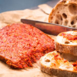 Kalabrische ’Nduja – die würzige, streichfähige Rohwurst – angerichtet auf knusprigem Bauernbrot mit rustikaler Kruste und lockerer Krume, bereit für den perfekten Antipasto-Moment.