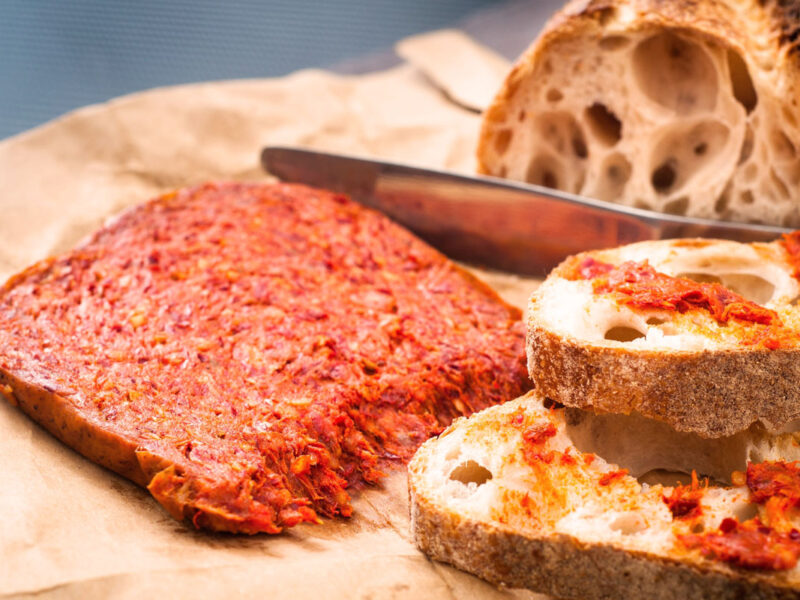 Kalabrische ’Nduja – die würzige, streichfähige Rohwurst – angerichtet auf knusprigem Bauernbrot mit rustikaler Kruste und lockerer Krume, bereit für den perfekten Antipasto-Moment.