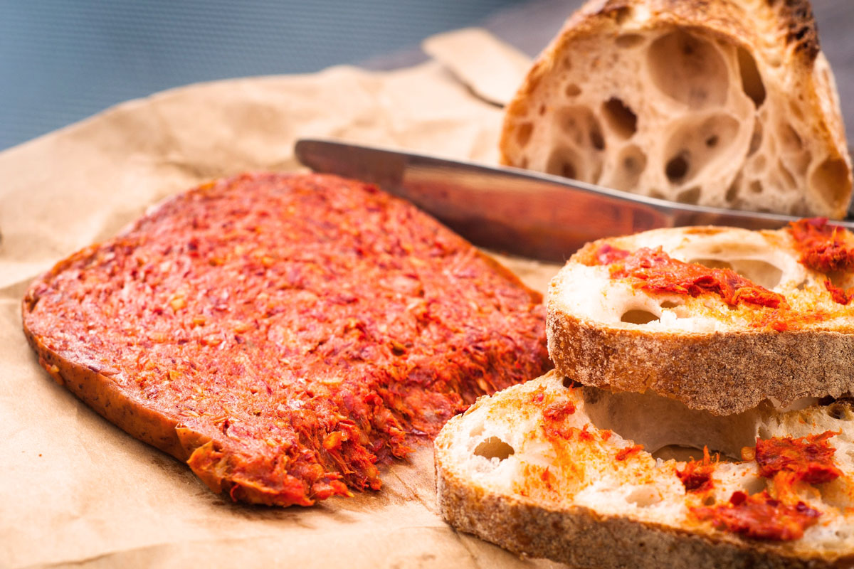 Kalabrische ’Nduja – die würzige, streichfähige Rohwurst – angerichtet auf knusprigem Bauernbrot mit rustikaler Kruste und lockerer Krume, bereit für den perfekten Antipasto-Moment.