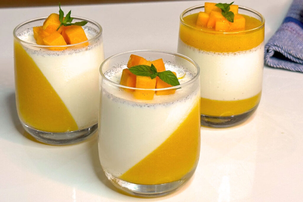 Dreierlei Gläser mit kunstvoll geschichteter Panna Cotta und Mangopüree, garniert mit frischer Minze und Mangowürfeln – modern interpretiertes italienisches Dessert.