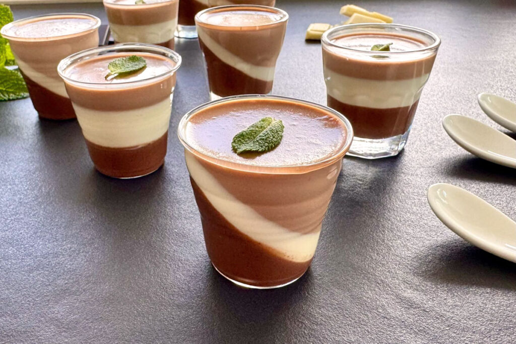 Zweifarbige Panna Cotta mit Schokoladen- und Vanilleschichten im Glas, kunstvoll diagonal geschichtet und mit Minzblatt garniert.