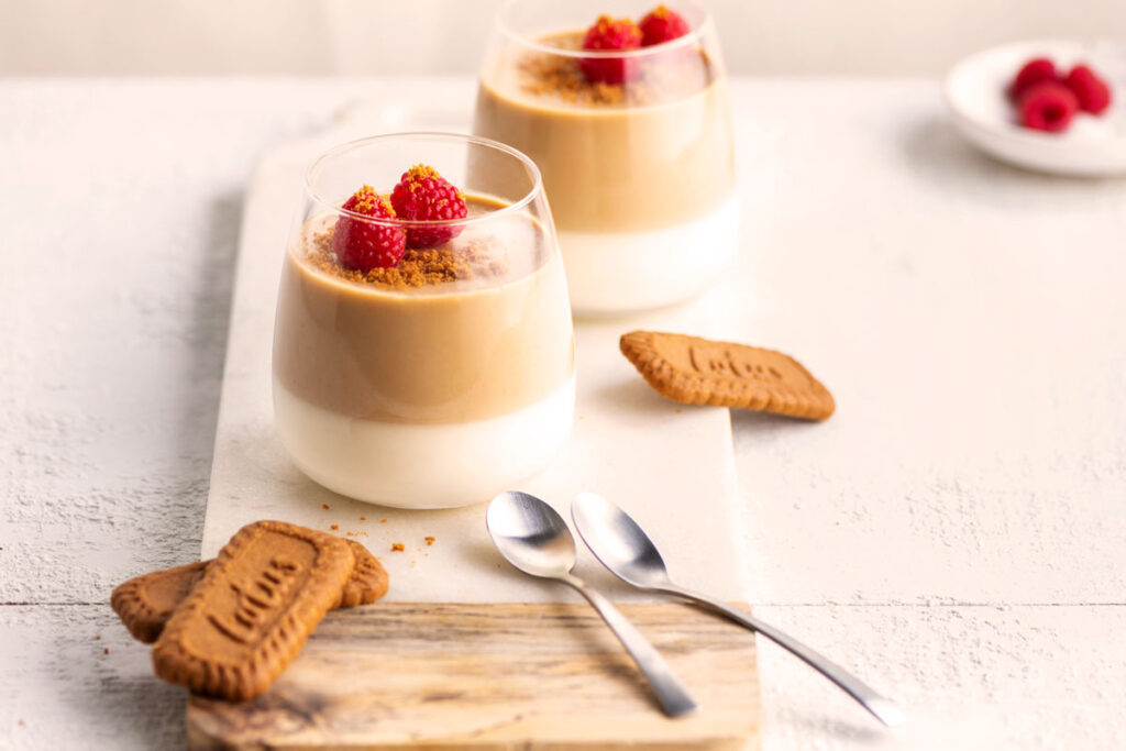 Panna Cotta mit Karamell- und Spekulatiuscreme, garniert mit Himbeeren und zerbröseltem Spekulatius, daneben Spekulatiuskekse.